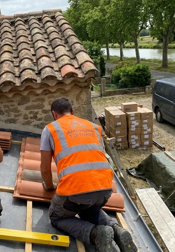 Couvreur Amphora Toitures alignant des tuiles canal sur liteaux, au bord d’un toit en tuiles anciennes à Sallèles-d’Aude